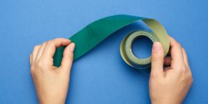 Zwei Hände halten für einen Workshop ein grünes Tape auf blauem Hintergrund
